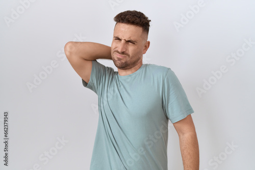 Hispanic man with beard standing over white background suffering of neck ache injury, touching neck with hand, muscular pain