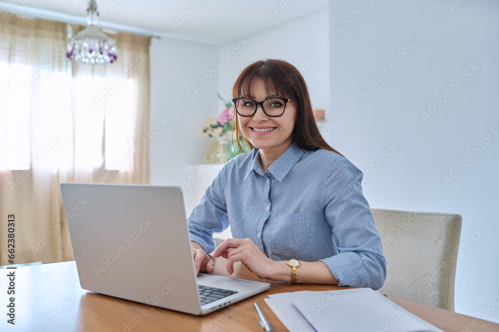 Middle aged business woman working at desk in home office, using laptop Middle aged business woman working at desk in home office, using laptop