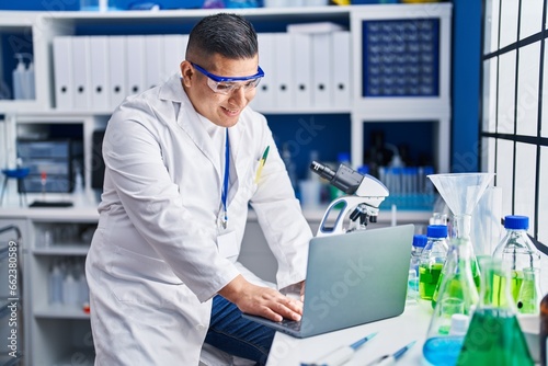 Young latin man scientist smiling confident using laptop at laboratory