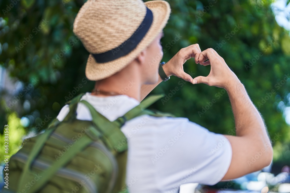 Young caucasian man tourist doing heart gesture with hands at park