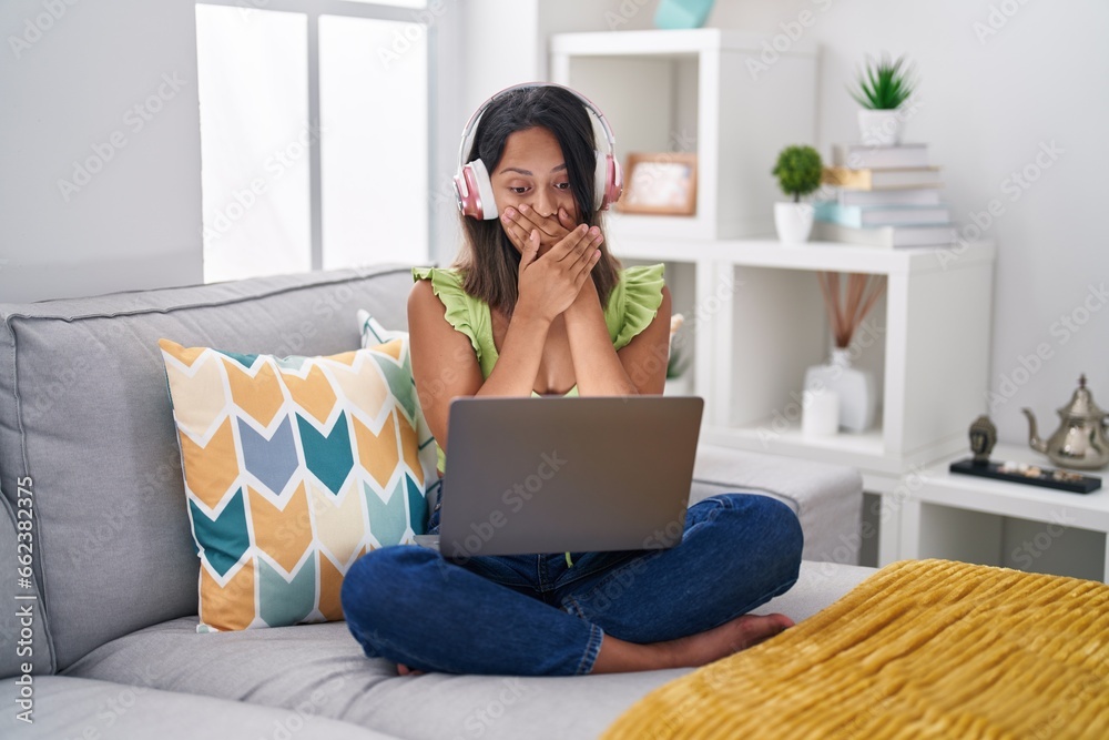 Hispanic young woman using laptop at home shocked covering mouth with hands for mistake. secret concept. Hispanic young woman using laptop at home shocked covering mouth with hands for mistake. secret concept.