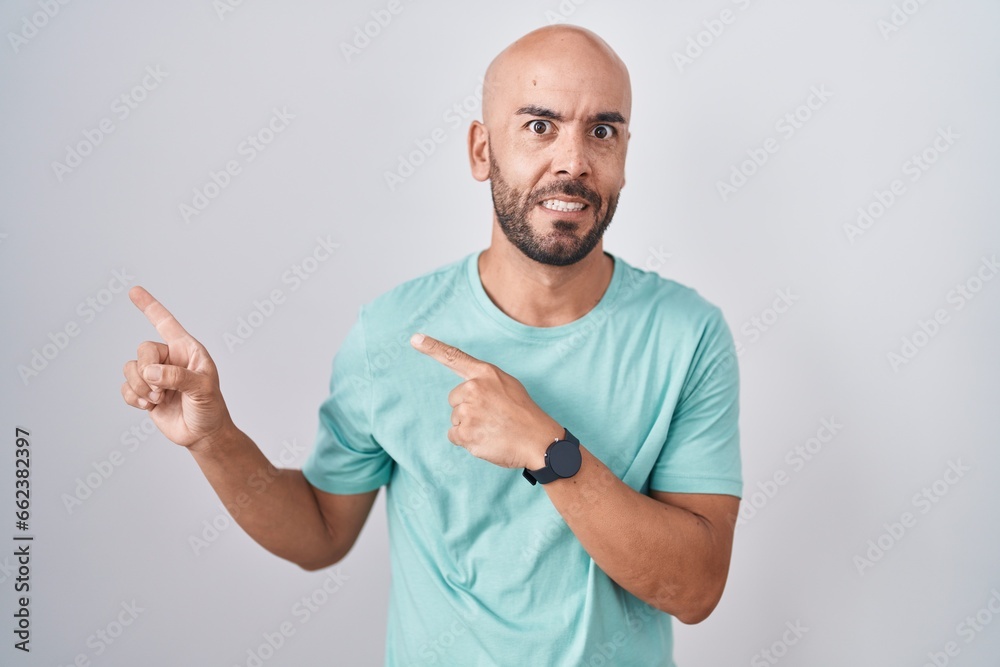 Middle age bald man standing over white background pointing aside worried and nervous with both hands, concerned and surprised expression Middle age bald man standing over white background pointing aside worried and nervous with both hands, concerned and surprised expression