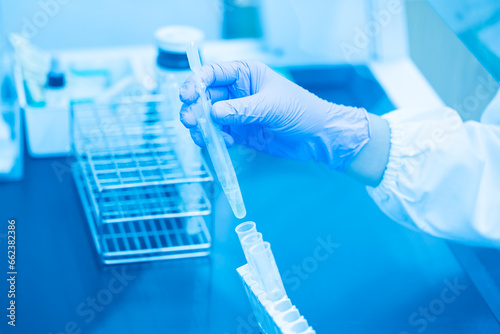 Close up scientist wearing blue gloves working with test tube in the flume hood at laboratory.Selective focus scientist hand holding sample blood test tube for fast laboratory at biochemistry unit.