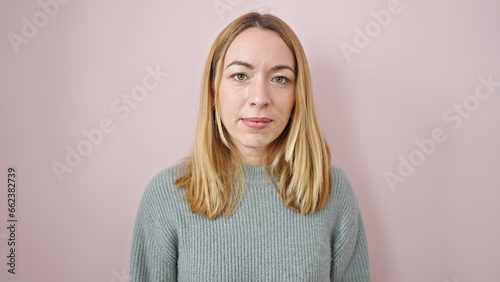 Young blonde woman standing with serious expression over isolated pink background © Krakenimages.com