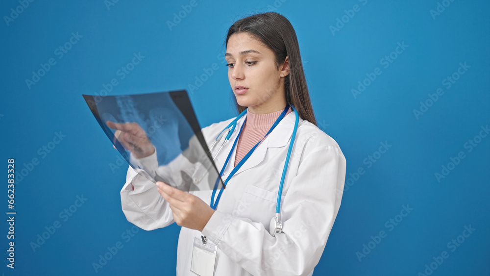 Young beautiful hispanic woman doctor looking xray over isolated blue background Young beautiful hispanic woman doctor looking xray over isolated blue background