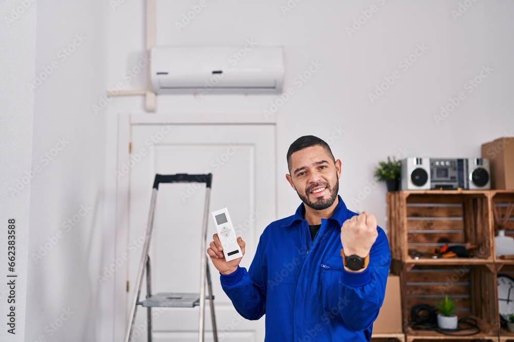 Hispanic repairman working with air conditioner screaming proud, celebrating victory and success very excited with raised arms