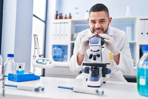 Young latin man scientist smiling confident using microscope at laboratory