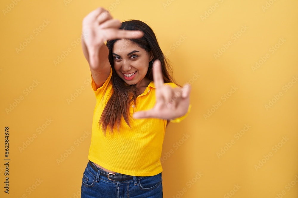 Young arab woman standing over yellow background smiling making frame with hands and fingers with happy face. creativity and photography concept. Young arab woman standing over yellow background smiling making frame with hands and fingers with happy face. creativity and photography concept.