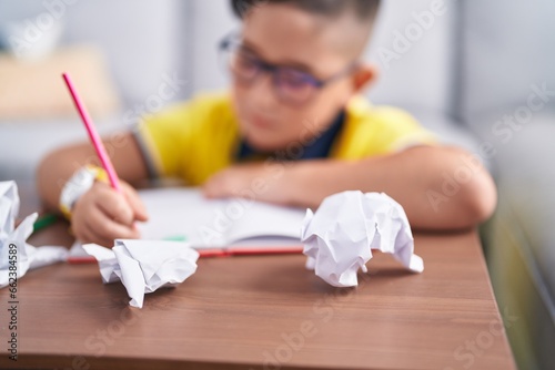 Adorable hispanic boy drawing on book sitting on floor at home