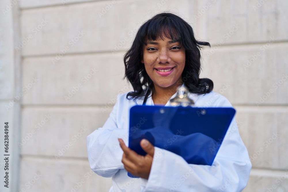 Young beautiful latin woman doctor smiling confident reading document at hospital Young beautiful latin woman doctor smiling confident reading document at hospital