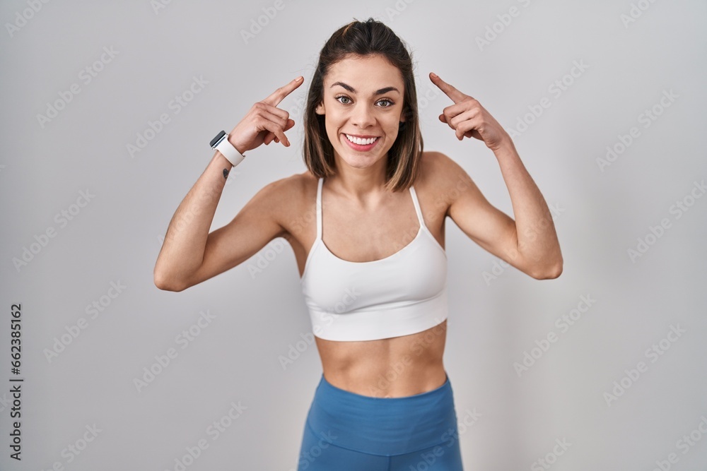 Hispanic woman wearing sportswear over isolated background smiling pointing to head with both hands finger, great idea or thought, good memory Hispanic woman wearing sportswear over isolated background smiling pointing to head with both hands finger, great idea or thought, good memory