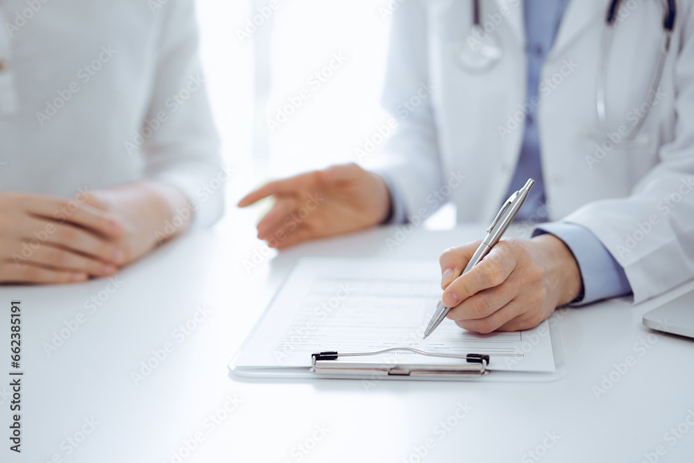Doctor and patient discussing current health questions while sitting near of each other and using clipboard at the table in clinic, just hands closeup. Medicine concept Doctor and patient discussing current health questions while sitting near of each other and using clipboard at the table in clinic, just hands closeup. Medicine concept