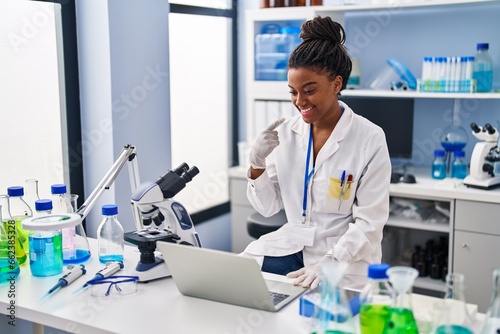 Young african american with braids working at scientist laboratory with laptop smiling happy pointing with hand and finger