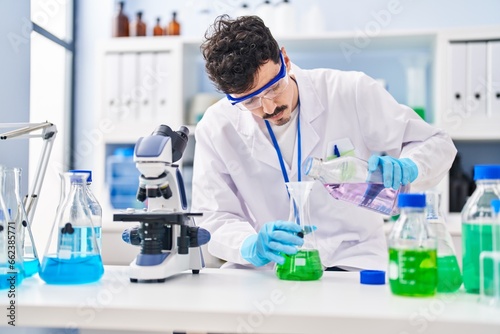 Young caucasian man scientist pouring liquid on test tube at laboratory
