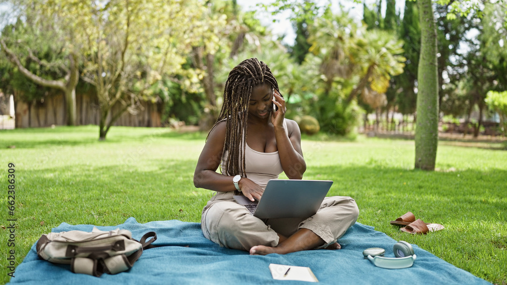 African american woman student using laptop talking on smartphone at campus university African american woman student using laptop talking on smartphone at campus university