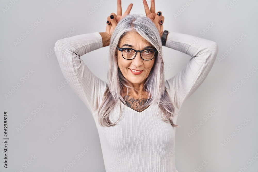 Middle age woman with grey hair standing over white background posing funny and crazy with fingers on head as bunny ears, smiling cheerful Middle age woman with grey hair standing over white background posing funny and crazy with fingers on head as bunny ears, smiling cheerful
