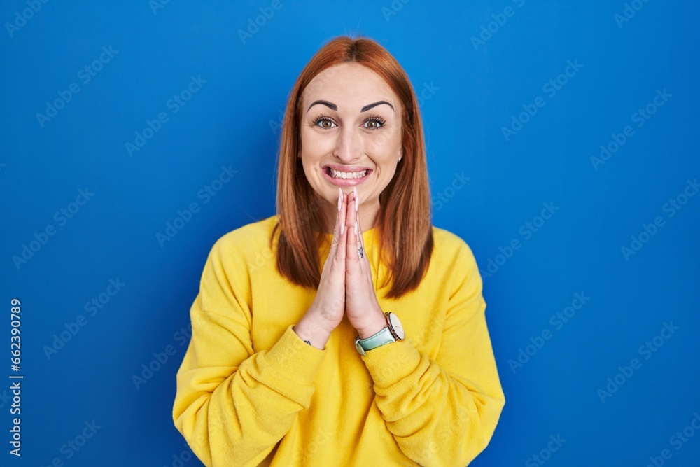 Young woman standing over blue background praying with hands together asking for forgiveness smiling confident. Young woman standing over blue background praying with hands together asking for forgiveness smiling confident.