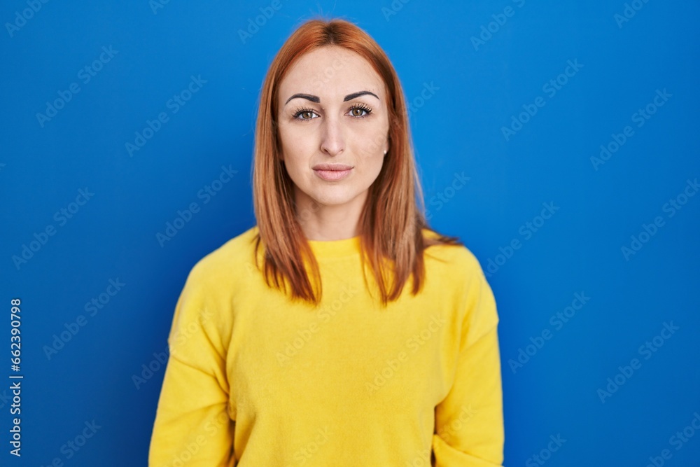 Young woman standing over blue background relaxed with serious expression on face. simple and natural looking at the camera. Young woman standing over blue background relaxed with serious expression on face. simple and natural looking at the camera.