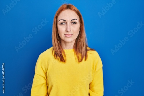 Young woman standing over blue background relaxed with serious expression on face. simple and natural looking at the camera.