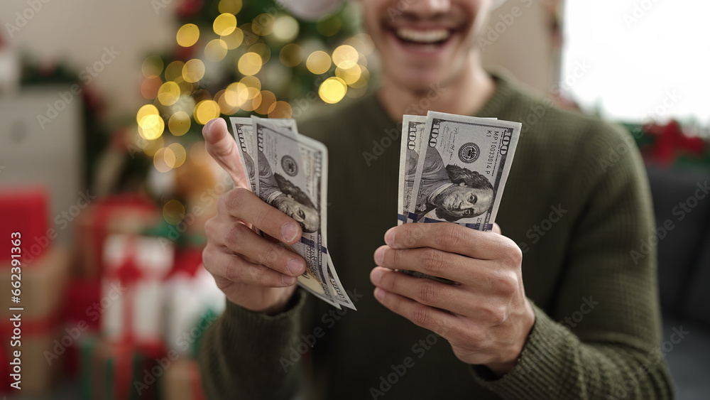 © Krakenimages.com - Young hispanic man counting dollars sitting on sofa by christmas tree at home © Krakenimages.com - Young hispanic man counting dollars sitting on sofa by christmas tree at home