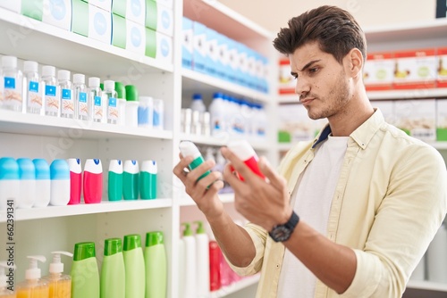 Young hispanic man customer holding toothpaste bottles at pharmacy