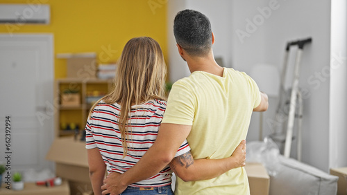 Man and woman couple hugging each other looking around standing backwards at new home