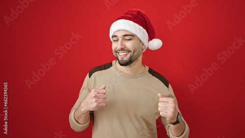 Young arab man wearing christmas hat dancing over isolated red background