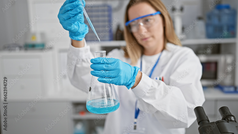 Gorgeous young blonde scientist in the lab, precision at work as she measures and pours liquid into a test tube for medical research Gorgeous young blonde scientist in the lab, precision at work as she measures and pours liquid into a test tube for medical research