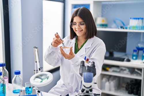 Young beautiful hispanic woman scientist smiling confident holding sample at laboratory