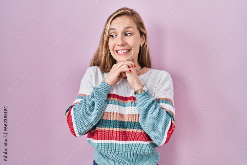 Young blonde woman standing over pink background laughing nervous and excited with hands on chin looking to the side Young blonde woman standing over pink background laughing nervous and excited with hands on chin looking to the side
