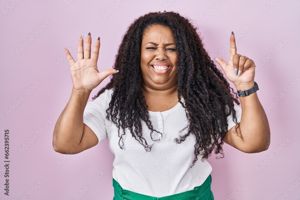 Plus size hispanic woman standing over pink background showing and pointing up with fingers number seven while smiling confident and happy. Plus size hispanic woman standing over pink background showing and pointing up with fingers number seven while smiling confident and happy.