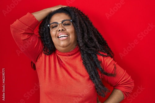 Plus size hispanic woman standing over red background smiling confident touching hair with hand up gesture, posing attractive and fashionable © Krakenimages.com