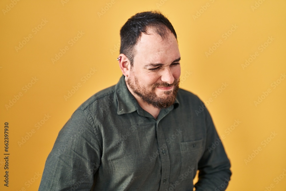 Plus size hispanic man with beard standing over yellow background with hand on stomach because indigestion, painful illness feeling unwell. ache concept. Plus size hispanic man with beard standing over yellow background with hand on stomach because indigestion, painful illness feeling unwell. ache concept.