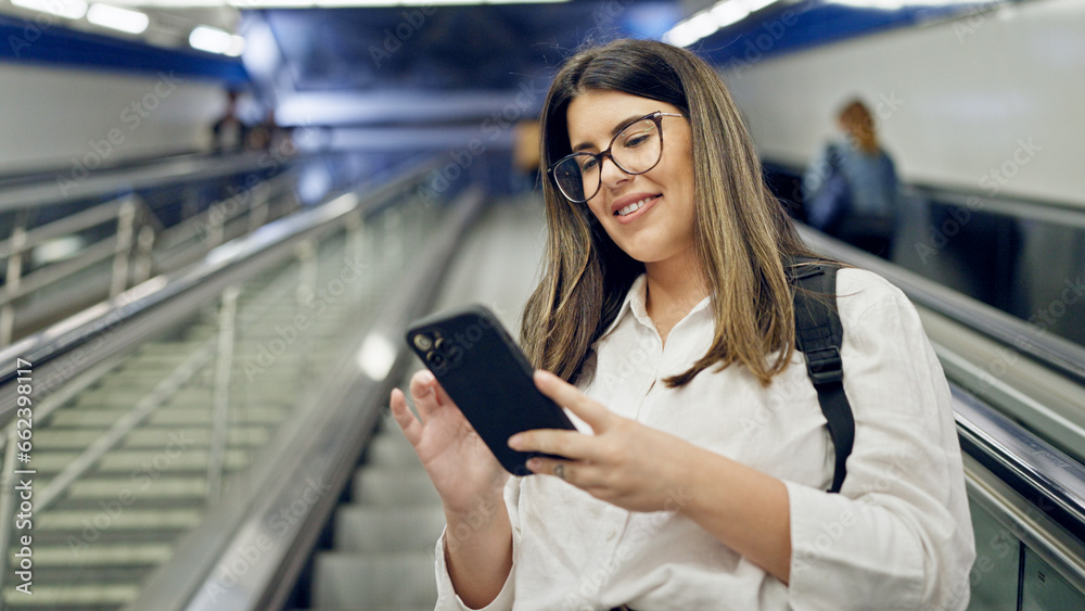 Young beautiful hispanic woman standing on escalator using smartphone in subway station of Madrid Young beautiful hispanic woman standing on escalator using smartphone in subway station of Madrid