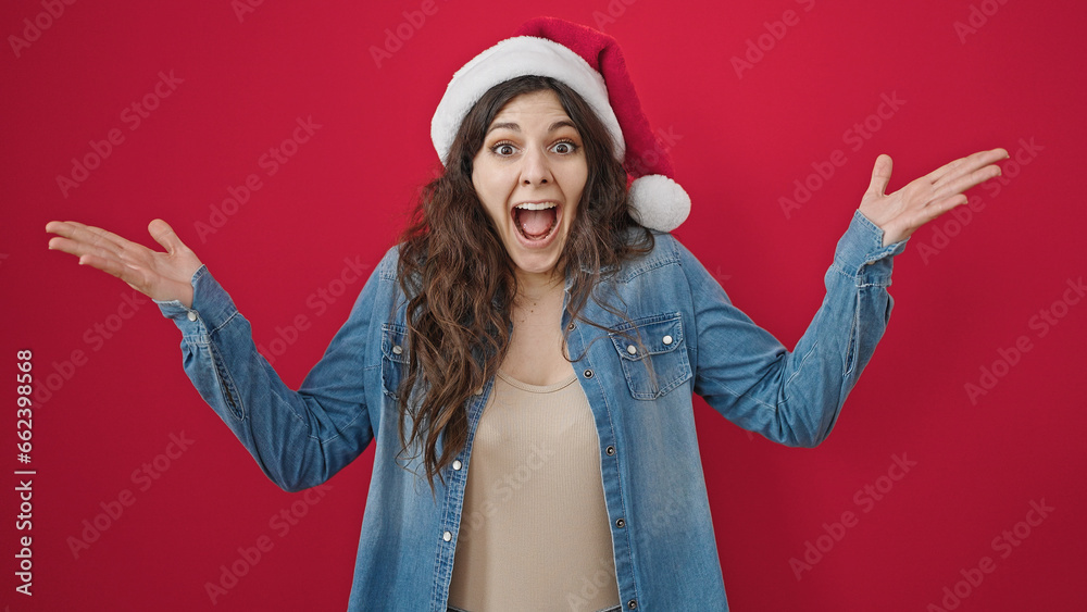 Young beautiful hispanic woman wearing christmas hat with surprise expression over isolated red background Young beautiful hispanic woman wearing christmas hat with surprise expression over isolated red background