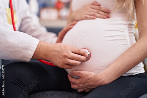 Man and woman doctor and pregnant patient auscultating baby at home