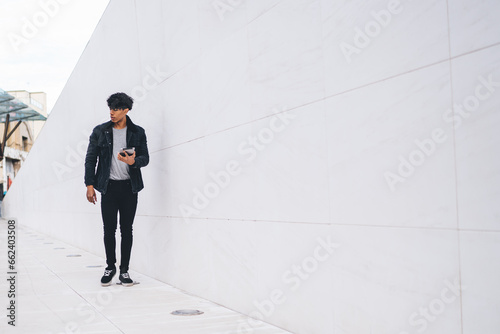 Casual ethnic man using tablet while walking along urban street tunnel
