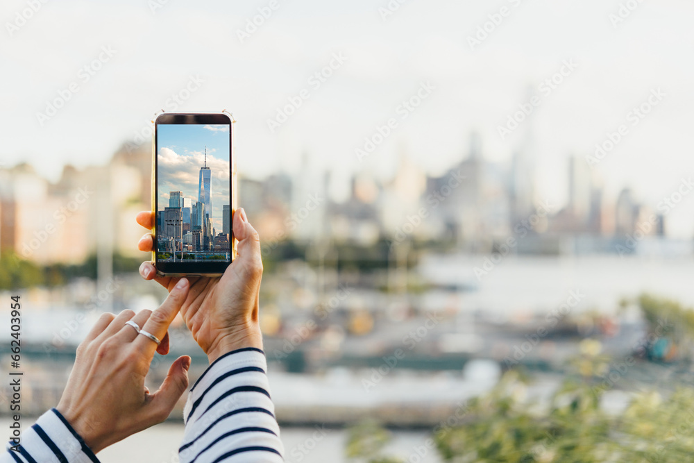 A person takes a mobile photo of the New York City's skyline seen from the bank of Hudson river at the West side of New York City, United States. - obrazy, fototapety, plakaty 
