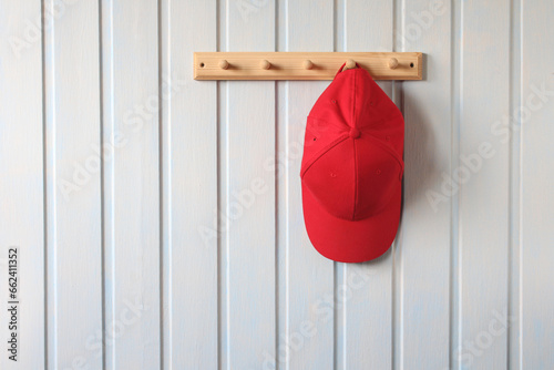 a red baseball cap is hanging on a wooden hanger on a white wall. natural background, empty space for your text.