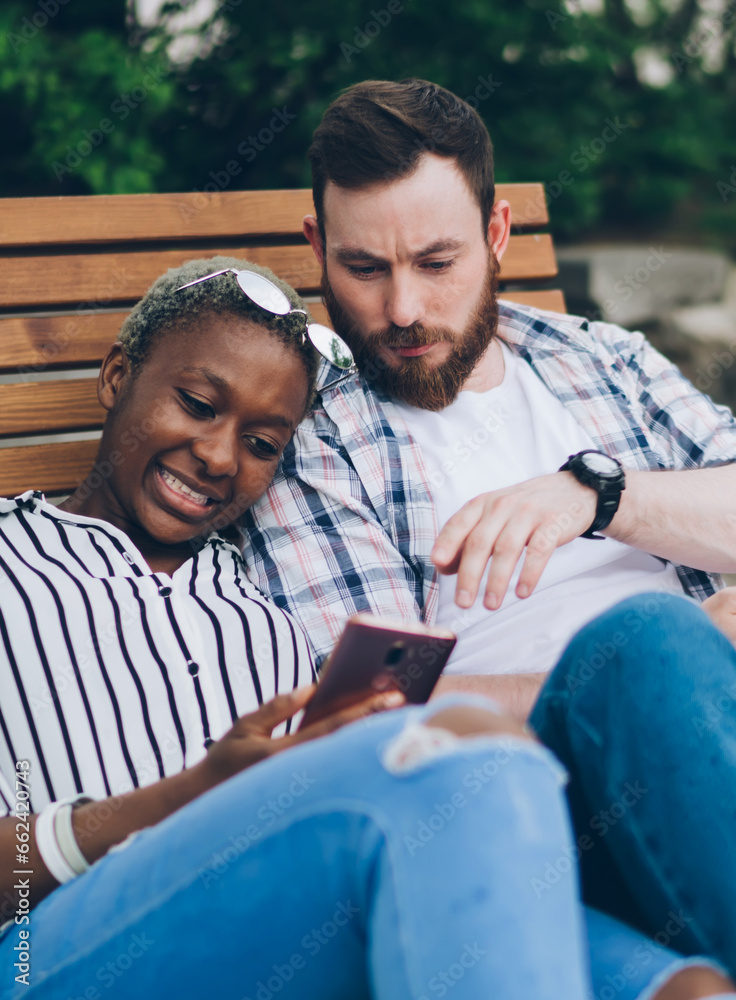 Fototapeta premium Pensive multiethnic couple using smartphones while resting in park