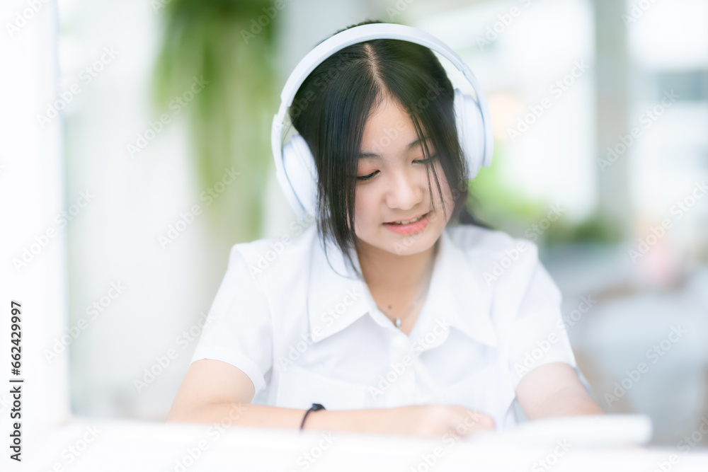 Happy of cute smiles Asian of attractive young Cute little girl wearing white wireless headphones and listening music enjoying favourite audio at the cafe on vacation at a coffee shop. Happy of cute smiles Asian of attractive young Cute little girl wearing white wireless headphones and listening music enjoying favourite audio at the cafe on vacation at a coffee shop.