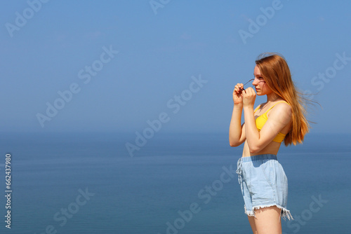 The girl is looking at the sea and puts on sunglasses