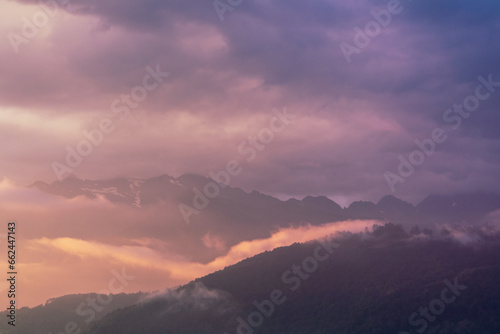 Fog and clouds in the mountains against the backdrop of the setting sun  changeable weather in the mountains  clouds and nebula on mountain peaks