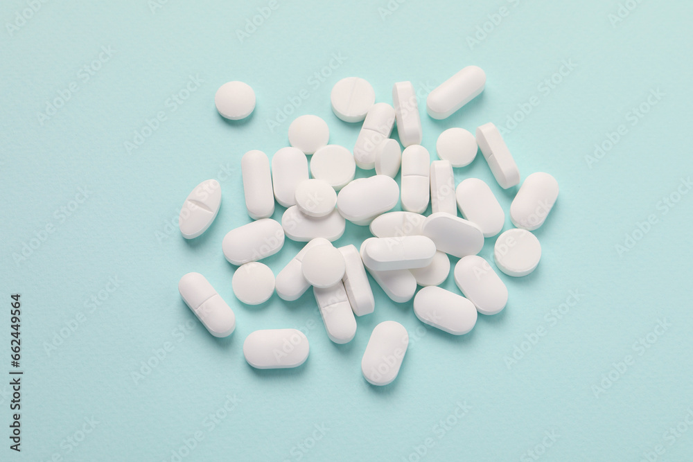Pile of white pills on mint background, flat lay