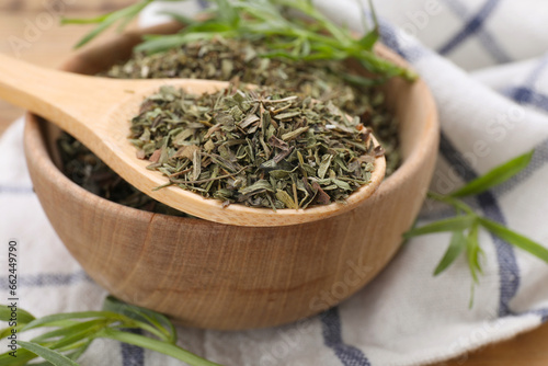 Bowl of dry tarragon and spoon on wooden table, closeup