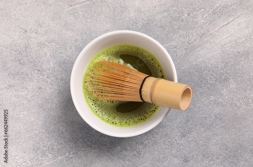 Cup of matcha tea and bamboo whisk on light gray textured table, top view