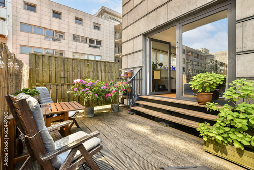a wooden deck with chairs and potted plants in the foreground, on a sunny day at an apartment building