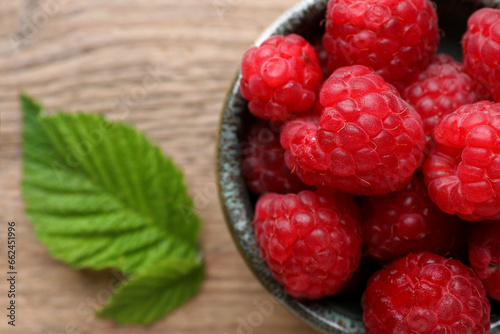 Tasty ripe raspberries and green leaves on wooden table, top view. Space for text