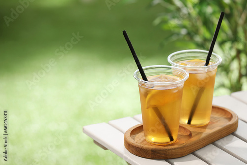 Plastic cups of tasty iced tea with lemon on white wooden table against blurred background, space for text