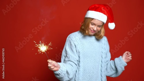 funny girl in Santa Claus cap holding sparkler on the red background. Concept Christmas